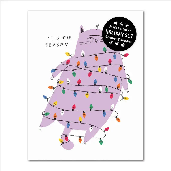 white greeting card with a purple cat tanged up in holiday christmas lights with a sour look on its face