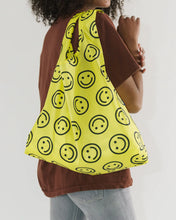 Load image into Gallery viewer,  a person holding an open baggu brand shopping reusable bag with the yellow happy face pattern 
