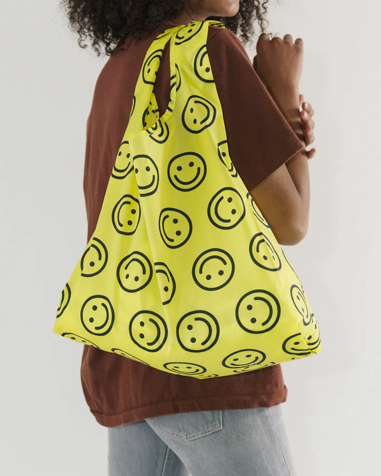  a person holding an open baggu brand shopping reusable bag with the yellow happy face pattern 