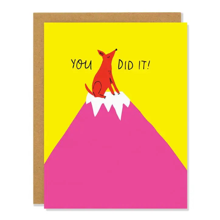 a yellow greeting card with a red dog standing on top of a mountain peak looking very proud. text you did it!